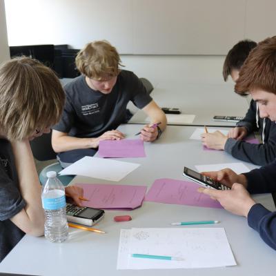 Four students use calculators and fill out worksheets at a table